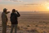Deux voyageurs observent au loin une installation spatiale dans la steppe kazakhe.
