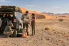 Des voyageurs vérifient leur carte et leur eau près d’un véhicule sur une piste désertique.